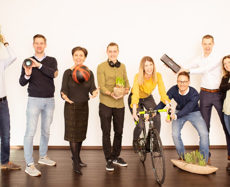 acht Menschen posieren mit verschiedenen Gegenständen