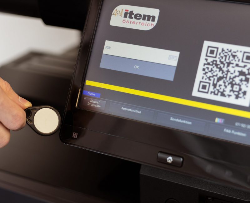 Das Bild zeigt die Authentifizierung an einem Kyocera-Drucksystem mithilfe eines RFID-Chips. Diese berührungslose Zugangsmethode unterstreicht den Fokus auf Sicherheit und Benutzerfreundlichkeit im modernen Dokumentenmanagement.