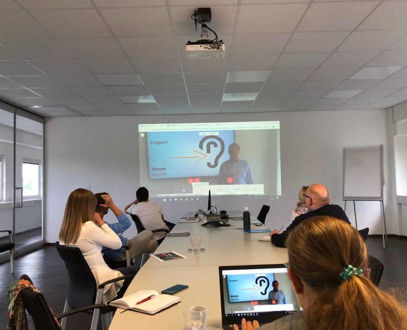 das Bild zeigt 6 Personen die auf einer Leinwand eine Präsentation gucken