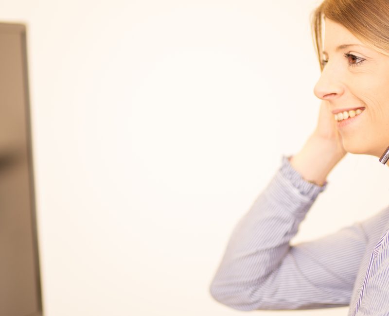 das Bild zeigt eine Frau mit einem Headset die vor einem Monitor sitzt